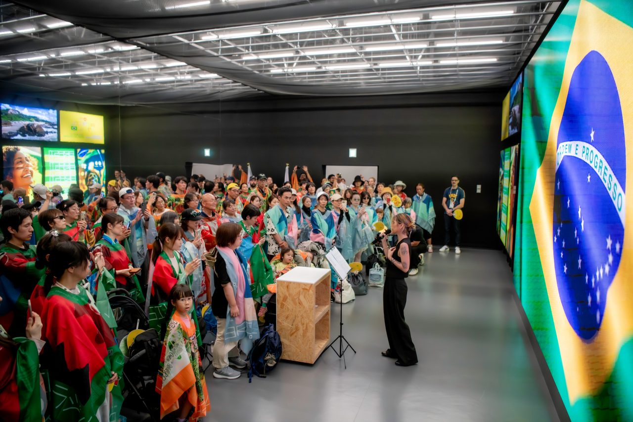 Palestrante e visitantes com bandeira nacional no Pavilhão do Brasil na Expo Osaka